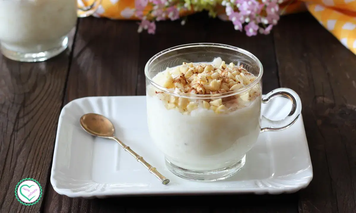 Una tazza di cremosa crema di riso, guarnita con mandorle tritate e cannella, pronta per essere gustata.