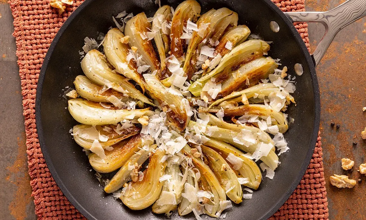 Finoçchi gratinati in padella, dorati e saporiti, guarniti con scaglie di formaggio e noci croccanti.