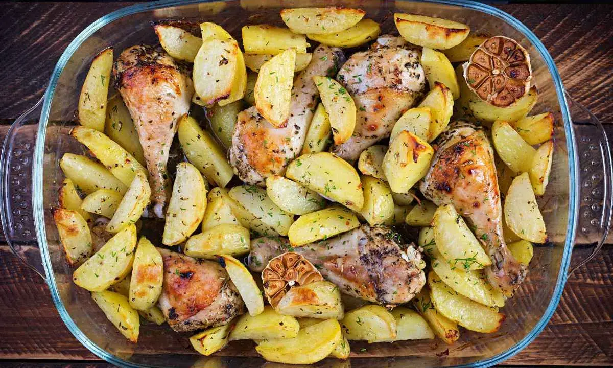Delizioso pollo al forno con patate, erbe aromatiche e spicchi d'aglio arrostiti, servito in una teglia di vetro.