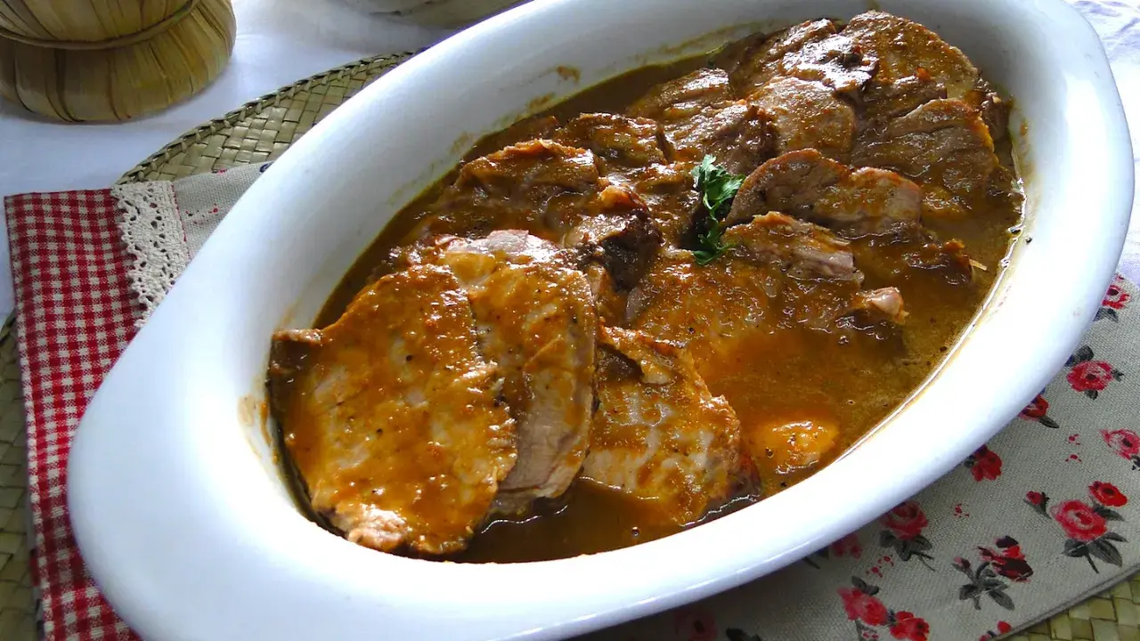Arrosto di maiale morbido con sughetto, servito in una teglia bianca, pronto per essere gustato.