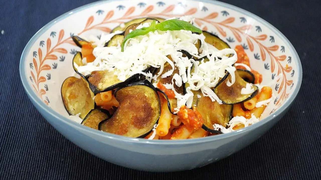 Un piatto di pasta alla norma fumante, con melanzane fritte, sugo rosso e abbondante ricotta salata grattugiata.