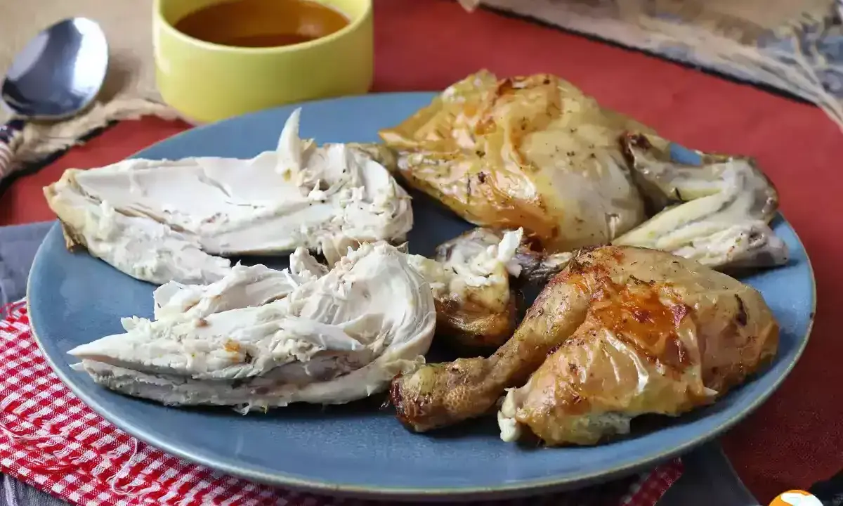 Piatto di petto di pollo arrosto succulento, tagliato a pezzi, con una ciotolina di salsa.