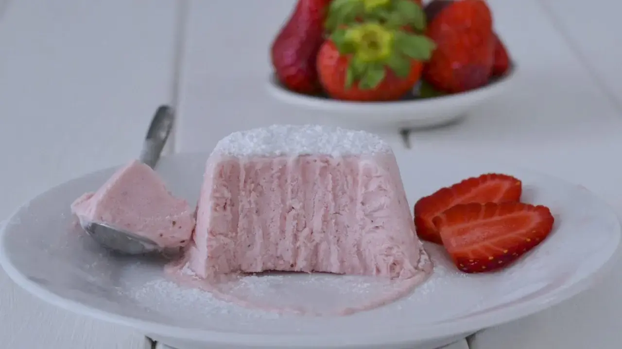 Delizioso semifreddo alle fragole, con una fetta servita su un cucchiaino e guarnito con zucchero a velo e fragole fresche.