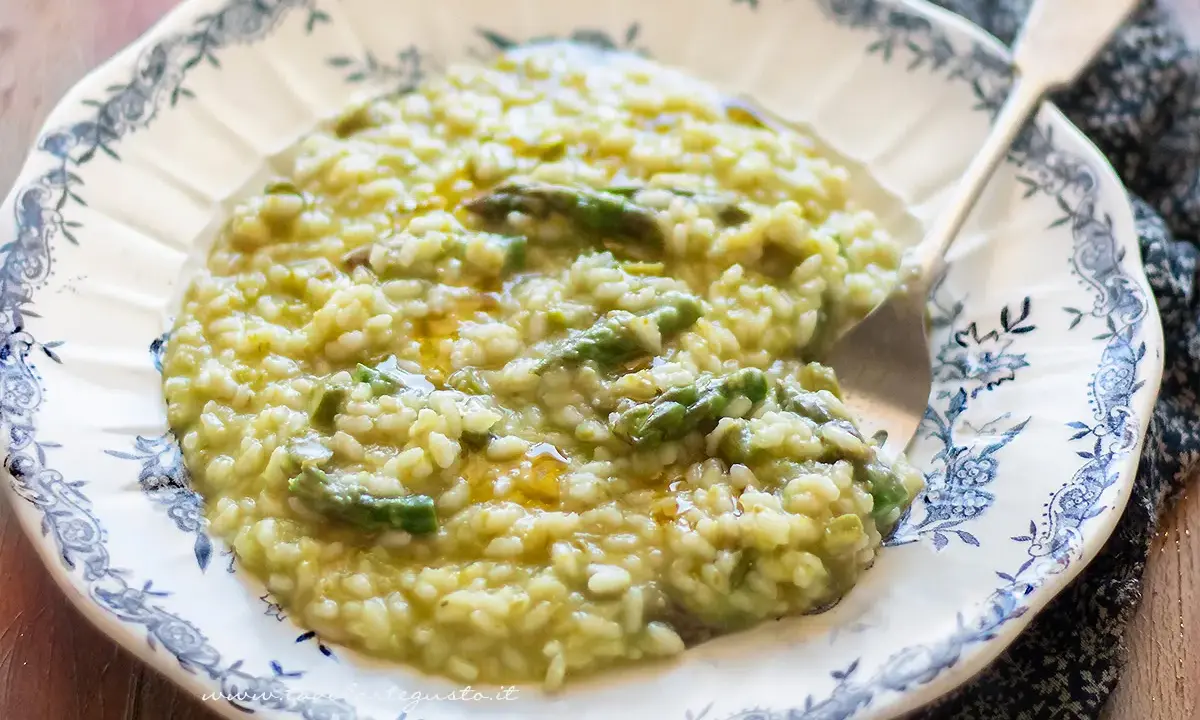 Un cremoso risotto con asparagi, servito in un piatto decorato. Un piatto primaverile che profuma di buono.