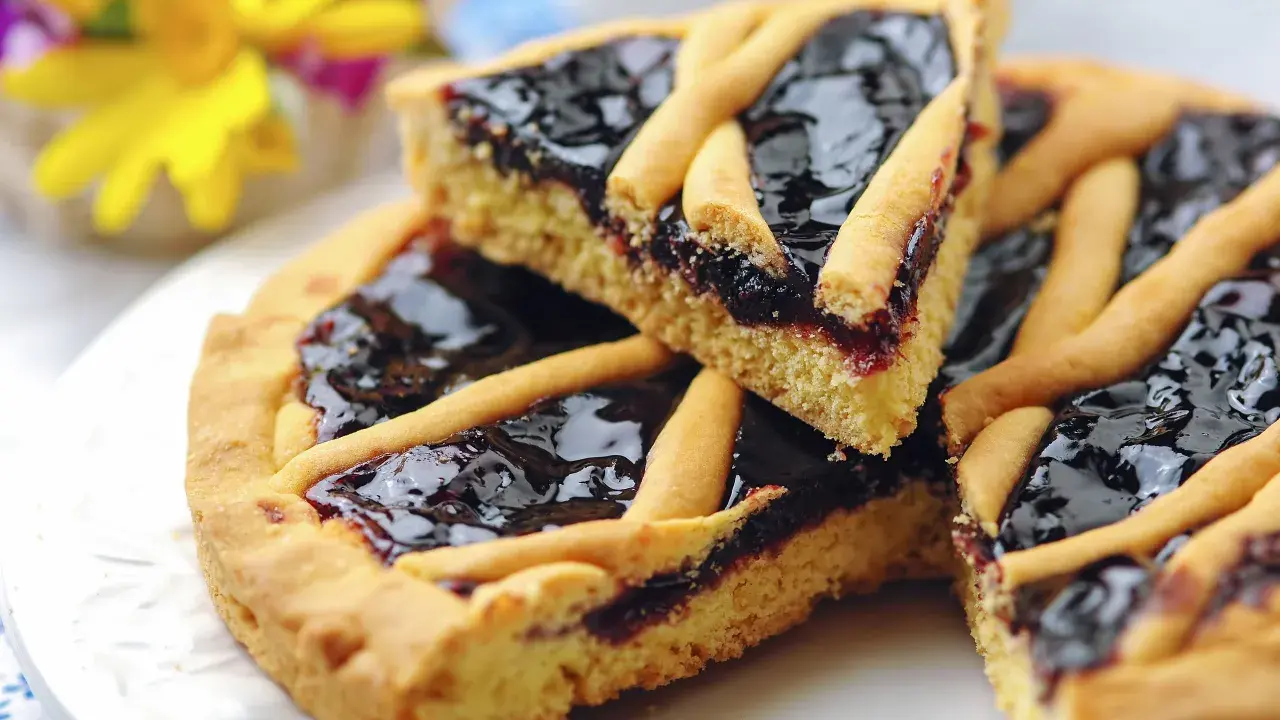 Una fetta di crostata di marmellata, con la sua pasta frolla dorata e il ripieno scuro e lucido, pronta per essere gustata.