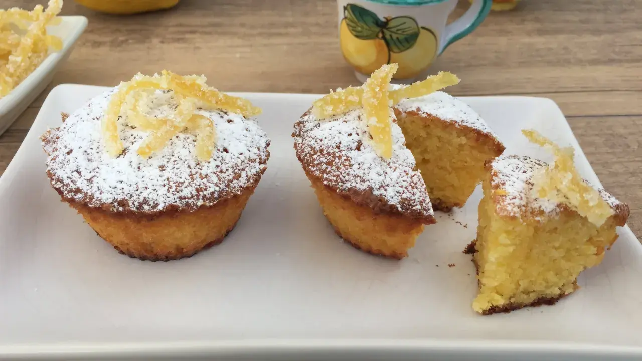 Deliziosi muffin caprese al limone, spolverati di zucchero a velo e decorati con scorzette candite.