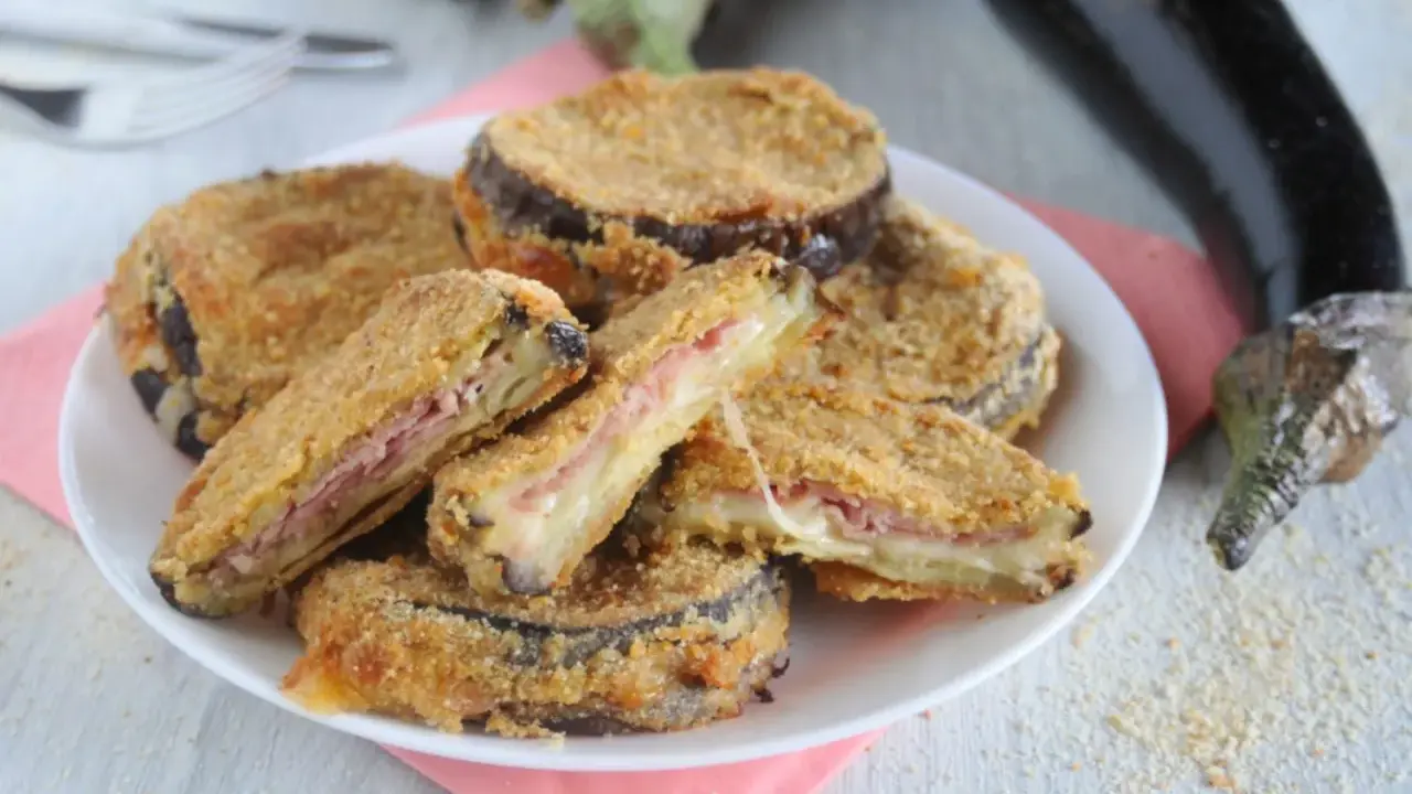 Cordon bleu di melanzane impanati e fritti, ripieni di prosciutto e formaggio filante, serviti su un piatto bianco.