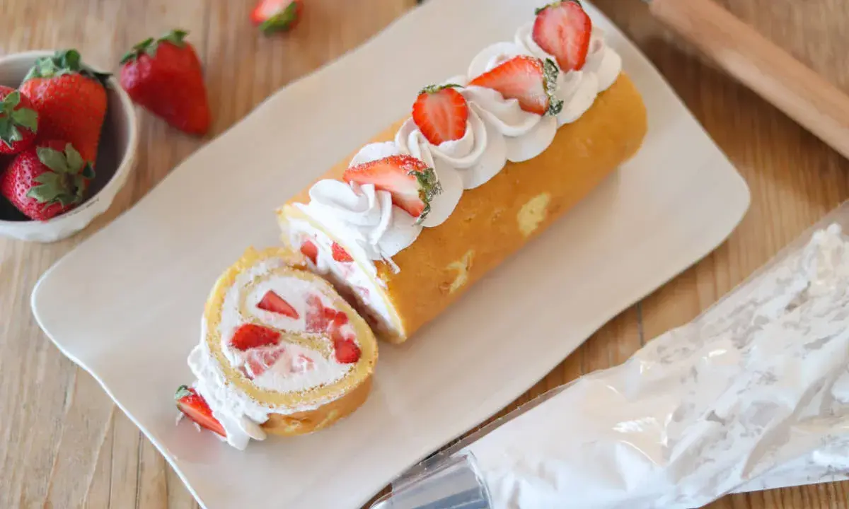 Rotolo panna e fragole decorato con panna montata e fragole fresche, pronto per essere gustato.
