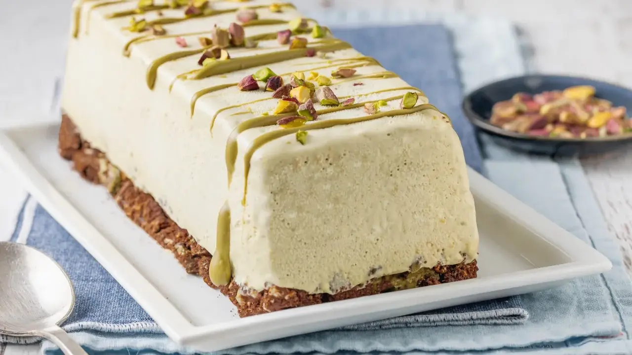 Semifreddo al pistacchio, un dolce gelato decorato con glassa verde e granella di pistacchi, su una base croccante.