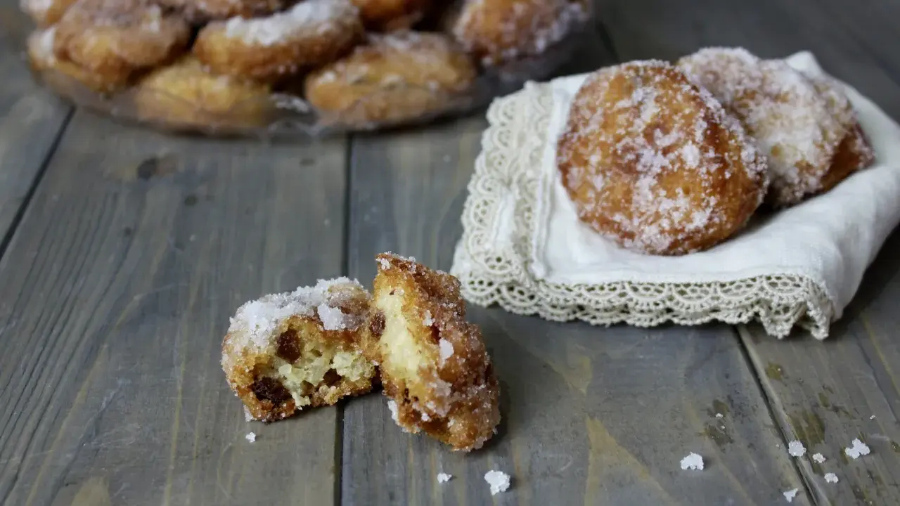 Frittelle di riso ricetta della nonna: dolcetti dorati e zuccherati, alcuni su un piatto, altri su un pizzo, uno aperto rivela l'interno morbido.