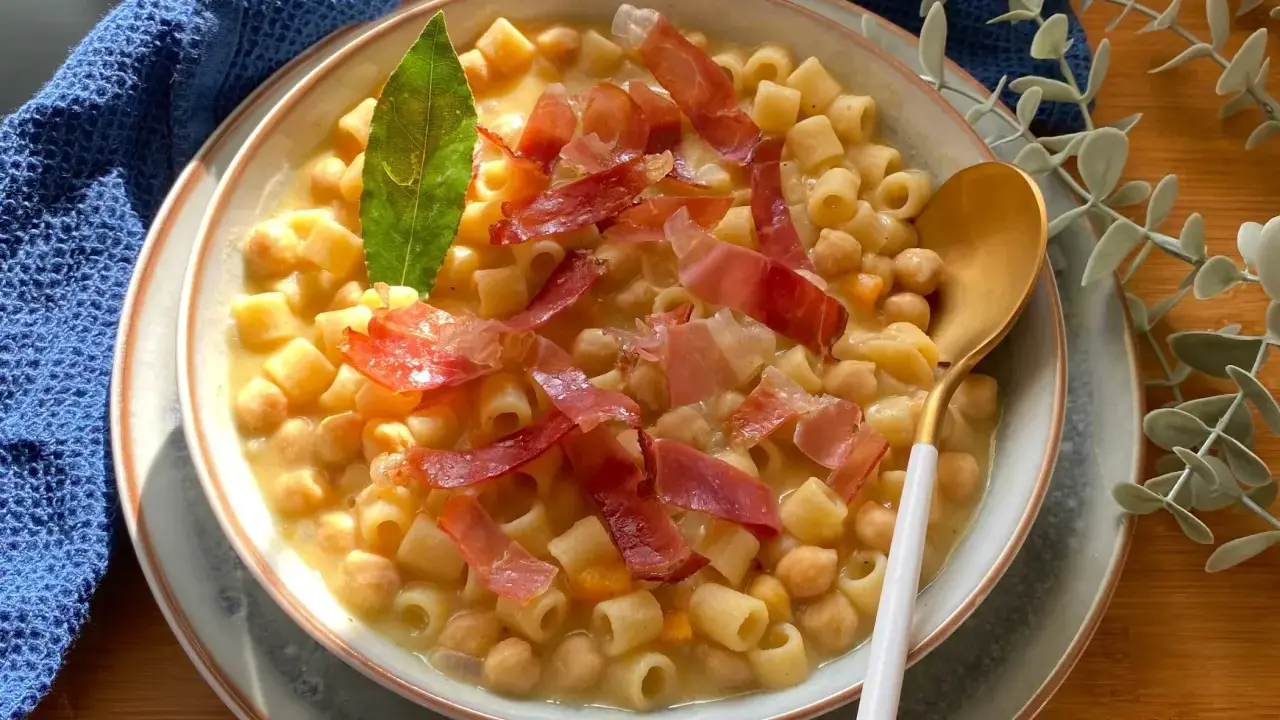 Un piatto fumante di pasta e ceci, arricchito da fette di prosciutto crudo e una foglia di alloro.
