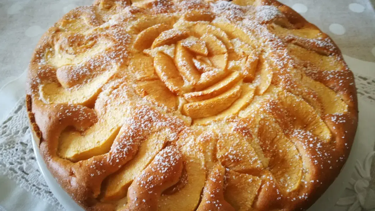 Una deliziosa torta di mele senza glutine, decorata con mele a forma di rosa e spolverata di zucchero a velo.