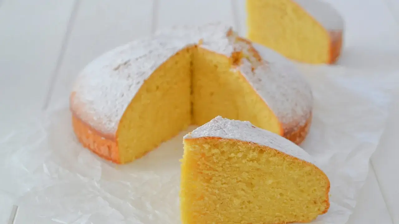 A fluffy lemon cake dusted with powdered sugar, with two slices cut out.