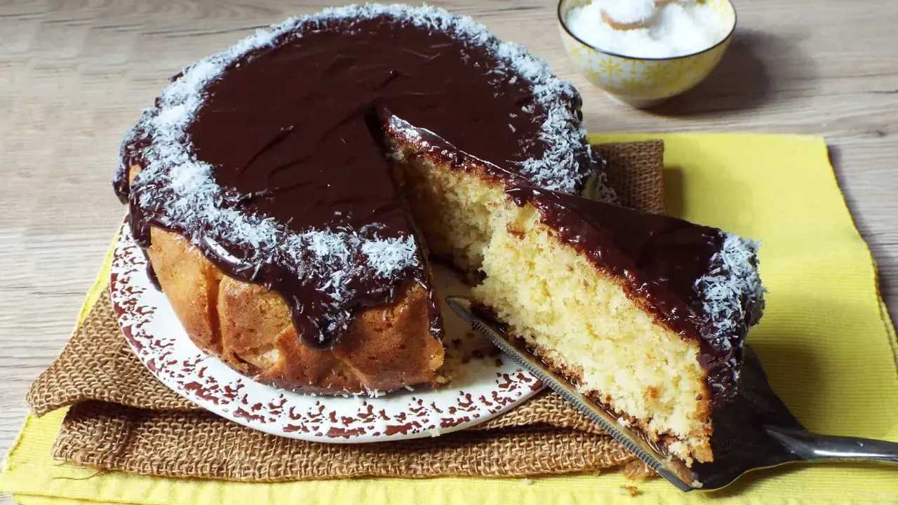 Deliziosa torta cocco e cioccolato, con una fetta appena tagliata e cosparsa di cocco grattugiato.