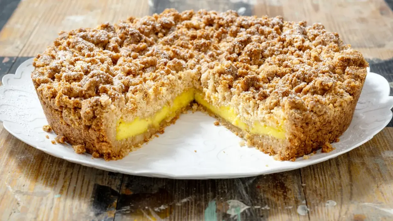 Sbriciolata alla crema con una crosta dorata e un ripieno giallo brillante, cosparsa di zucchero a velo.