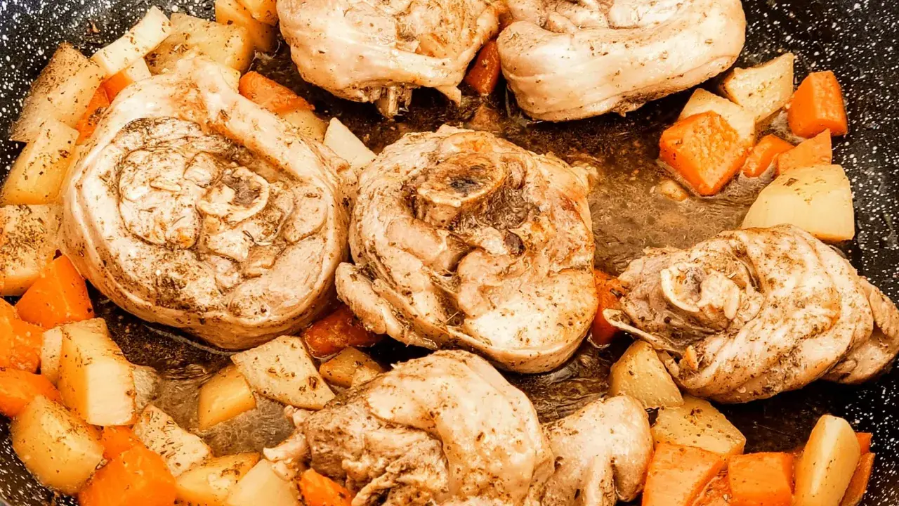 Porzioni di ossobuco di tacchino cotte in padella con patate e carote a cubetti, condite con erbe aromatiche.