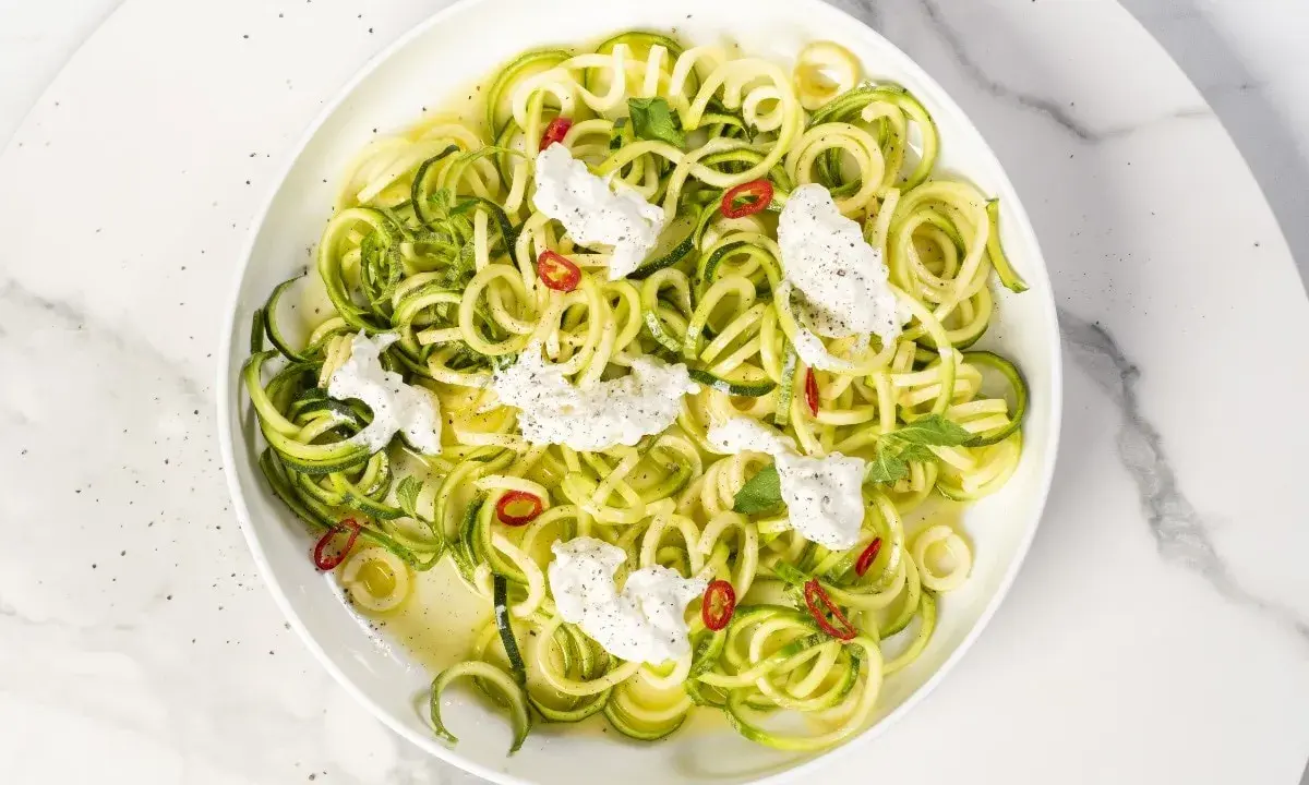 Spaghetti di zucchine freschi con ricotta cremosa, peperoncino e menta, un piatto leggero e colorato.