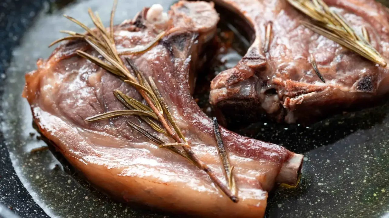 Due braciole di maiale succulente cuociono in padella con rametti di rosmarino.