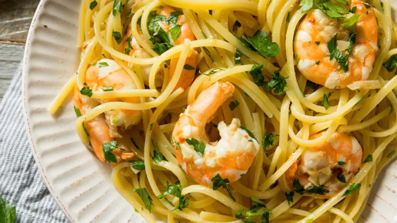Un piatto invitante di pasta con gamberetti, condita con prezzemolo fresco e servita su un piatto bianco.