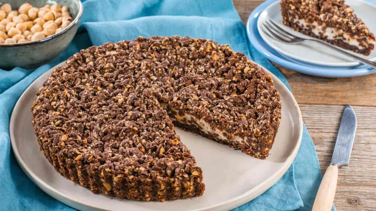 Sbriciolata ricotta e cioccolato con croccante copertura di nocciole. Una fetta è già servita su un piattino.