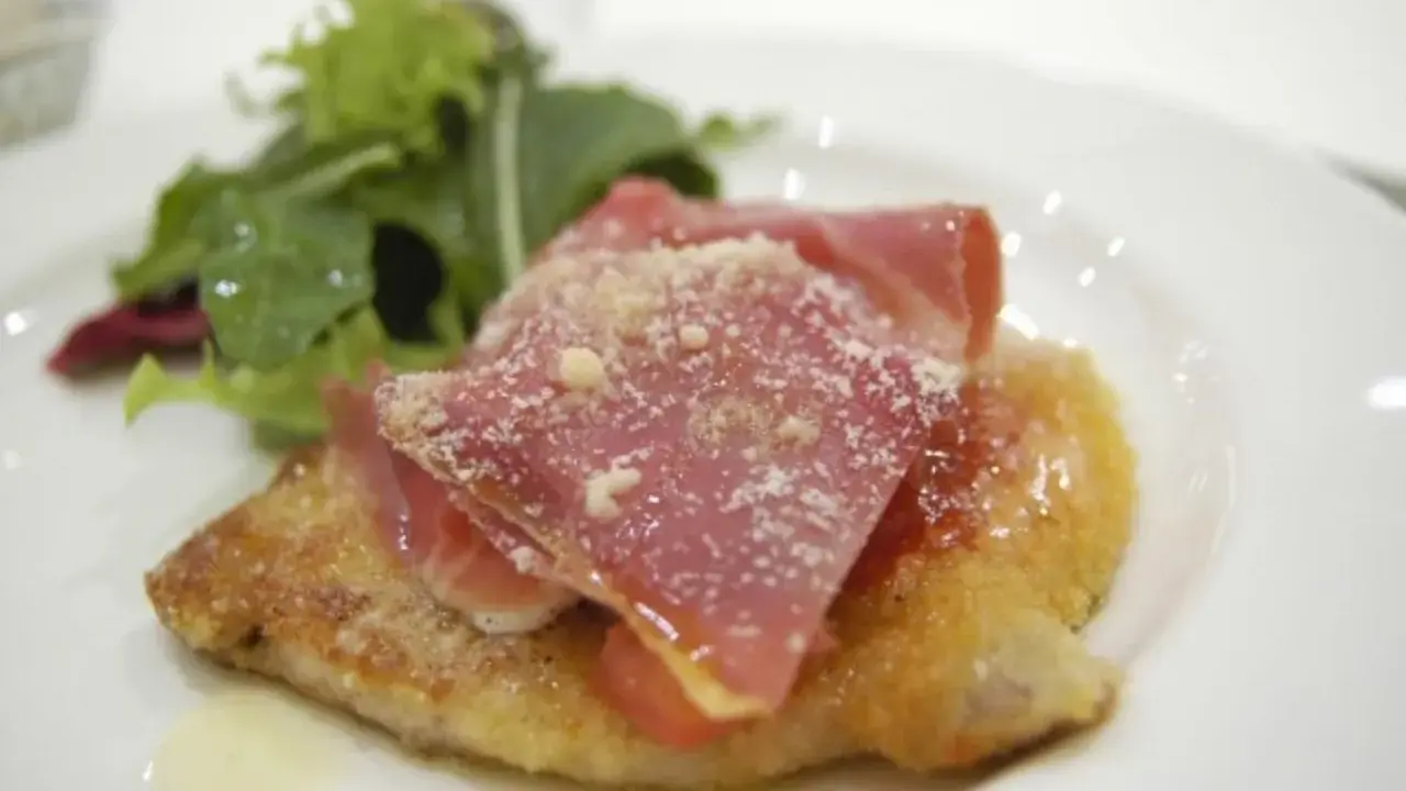 Cotoletta alla bolognese dorata, coperta da prosciutto crudo e parmigiano, con un contorno di insalata fresca.