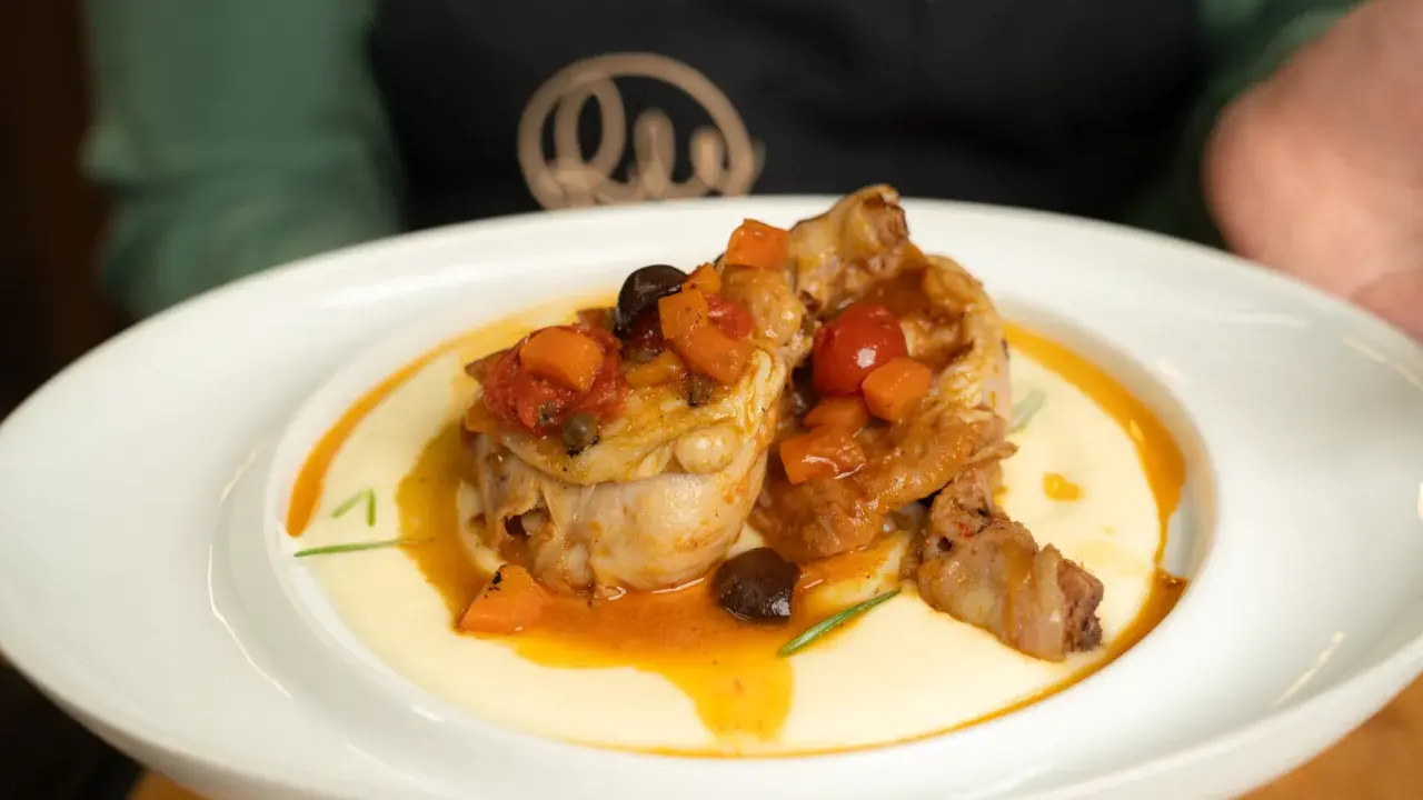 Pollo alla cacciatora ricetta della nonna: succulenti pezzi di pollo in umido con pomodoro, olive e carote, serviti su un letto di polenta cremosa.