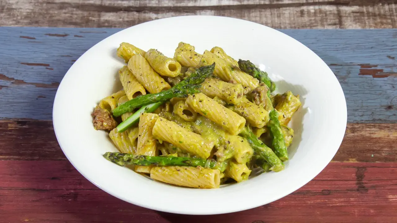 Piatto di pasta con asparagi e salsiccia, condita con una cremosa salsa verde.