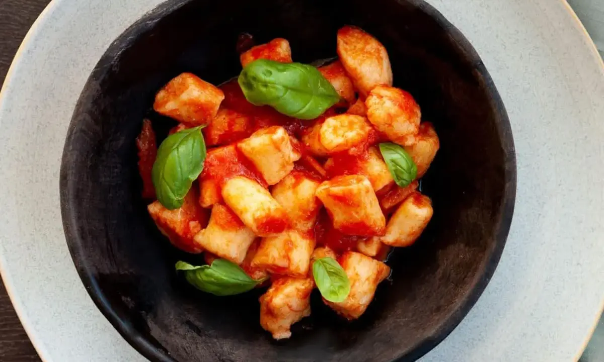 Gnocchi di ricotta soffici e saporiti, conditi con un sugo di pomodoro fresco e guarniti con foglie di basilico.