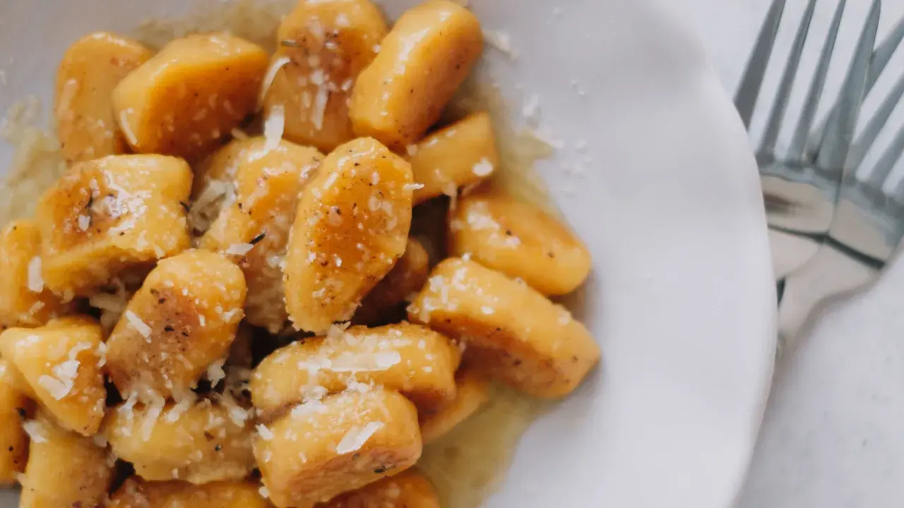 Gnocchi di zucca dorati, conditi con burro fuso, pepe nero e scaglie di parmigiano, pronti per essere gustati.