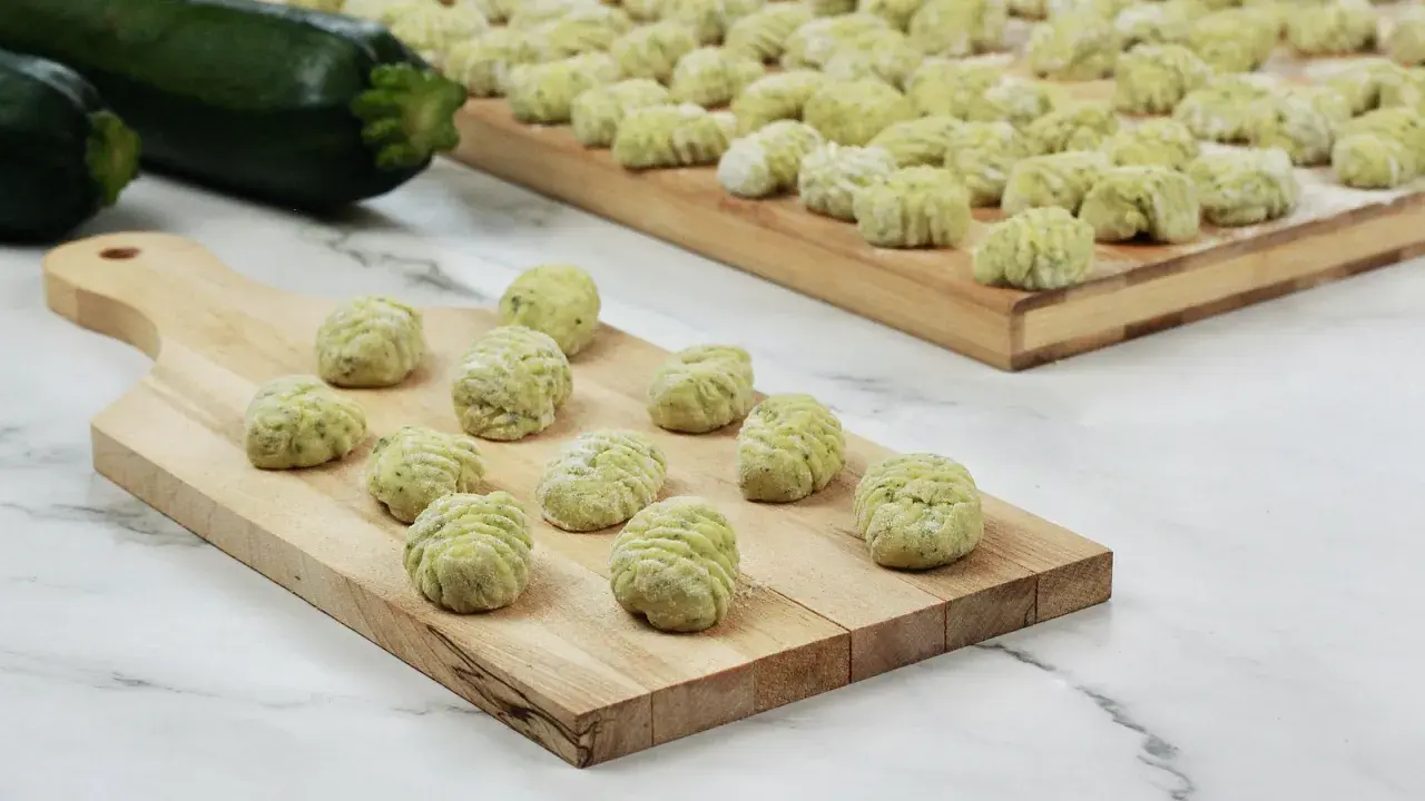 Gnocchi di zucchine freschi, pronti per essere cotti, disposti su taglieri di legno.