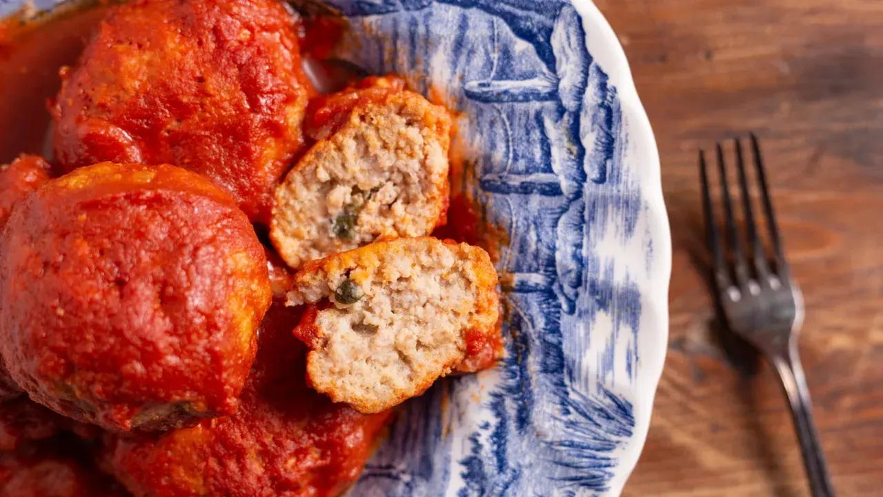 Polpette al sugo succulente in un piatto decorato, una tagliata rivela un interno morbido e saporito.
