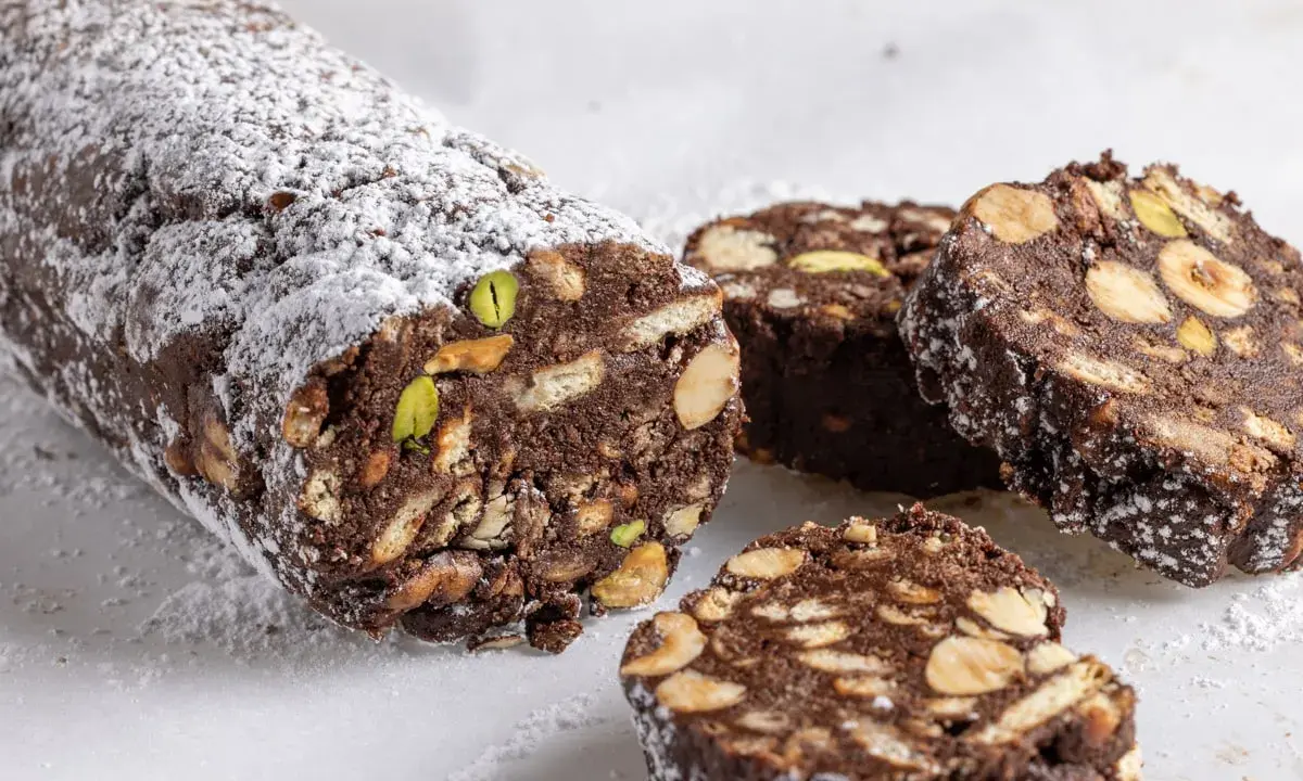 Salame di cioccolato senza uova, ricco di nocciole, mandorle e pistacchi, spolverato di zucchero a velo.