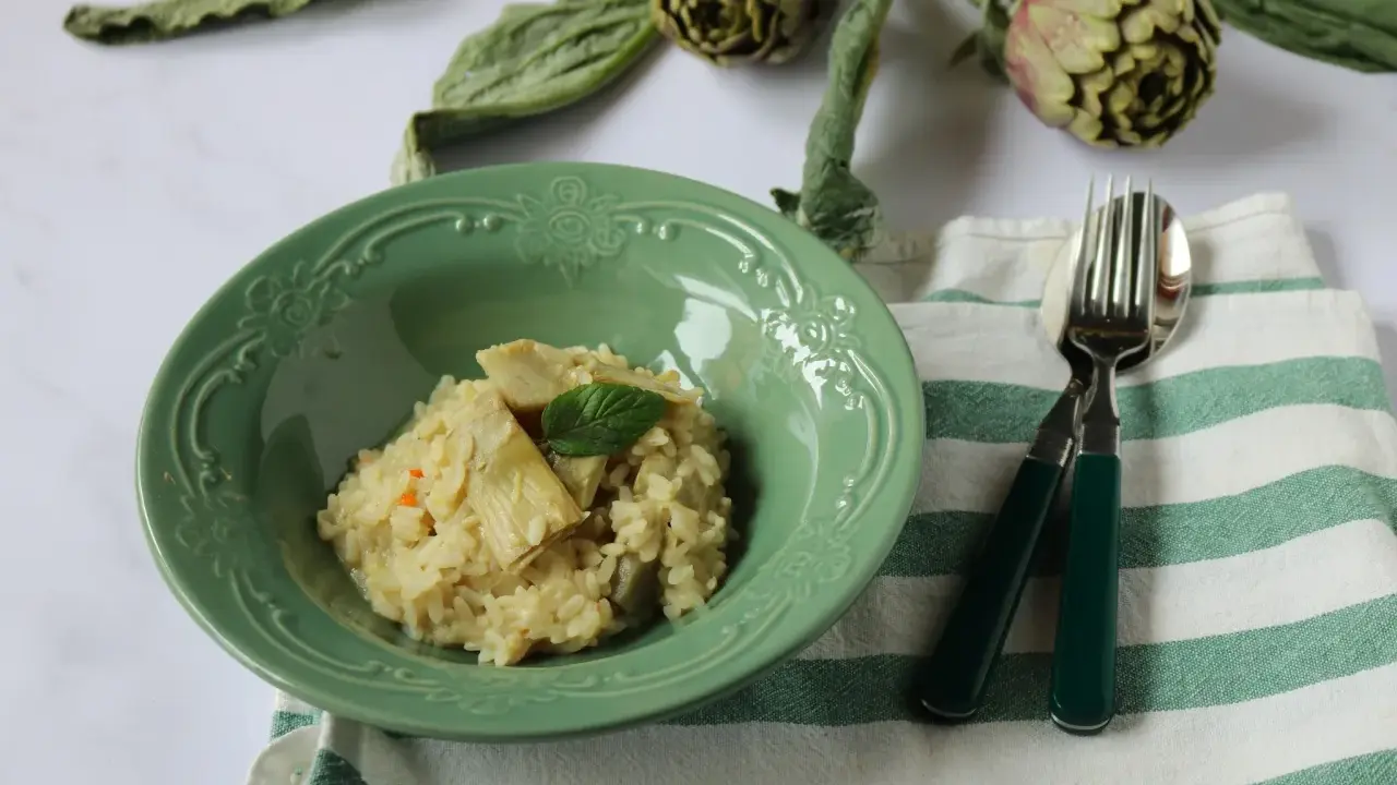 Un cremoso risotto con carciofi freschi, guarnito con una fogliolina di menta, pronto per essere gustato.