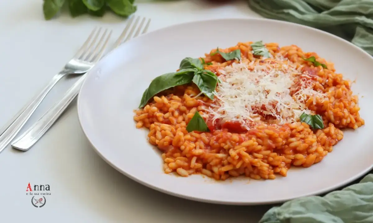 Un cremoso risotto al pomodoro, guarnito con basilico fresco e parmigiano grattugiato, pronto per essere gustato.
