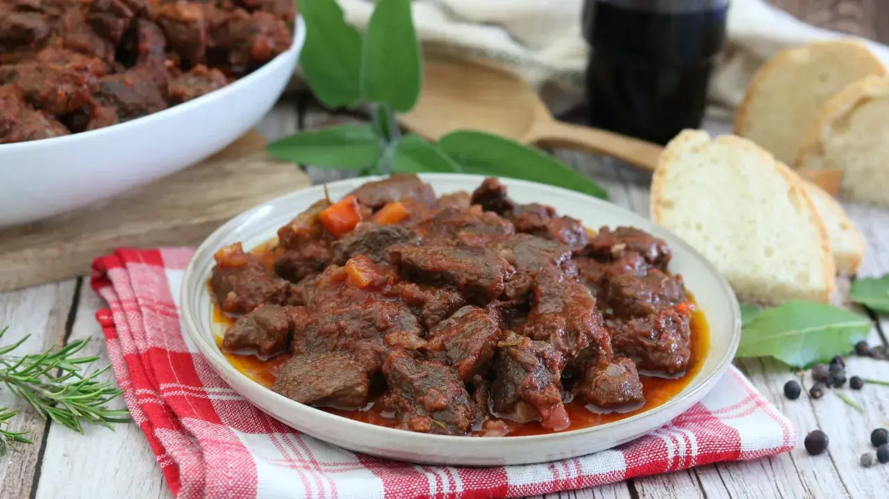 Cinghiale in umido fatto in casa da Benedetta, un piatto ricco e saporito, servito con pane fresco e un bicchiere di vino rosso.