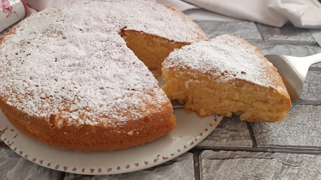 Una soffice torta al latte, spolverata di zucchero a velo, con una fetta appena tagliata pronta per essere gustata.
