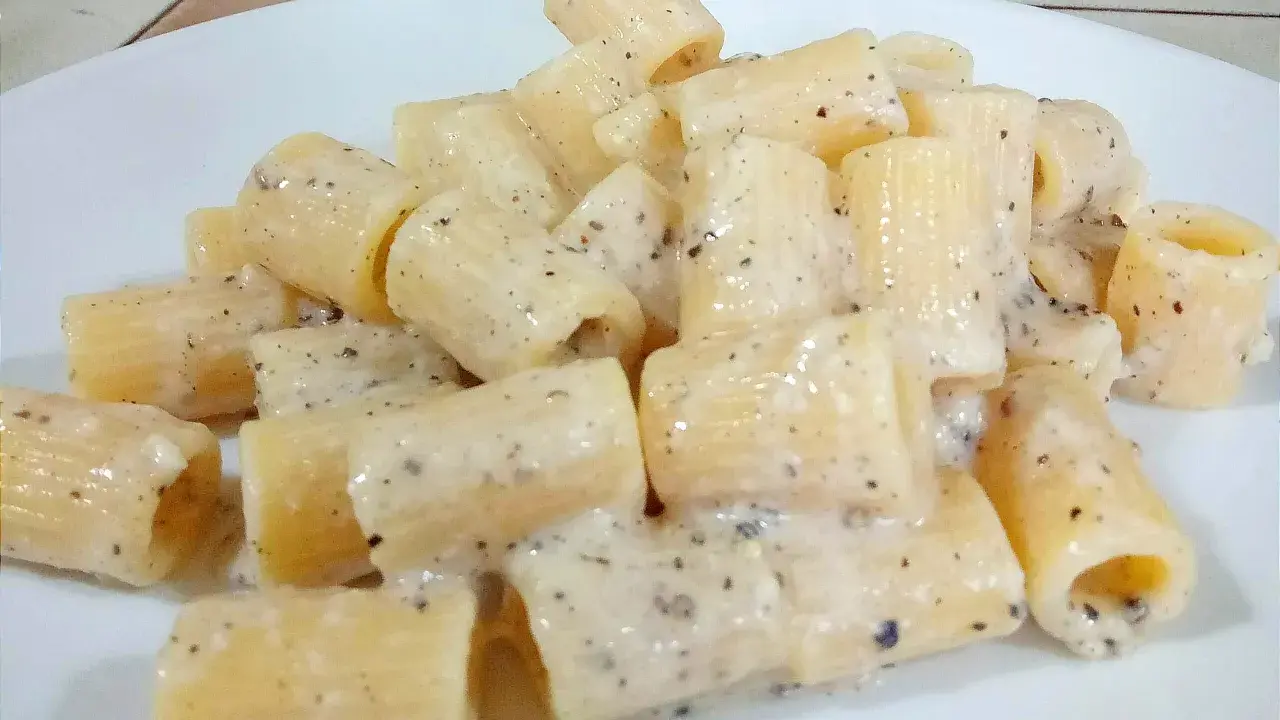 Piatto di rigatoni cremosi conditi con un classico cacio e pepe, pronti per essere gustati.
