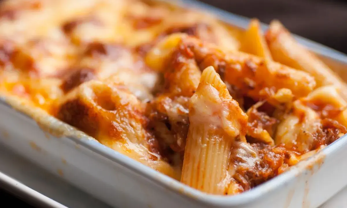Un invitante piatto di pasta pasticciata al forno, con penne ricoperte da un ricco sugo e formaggio filante, pronto per essere gustato.