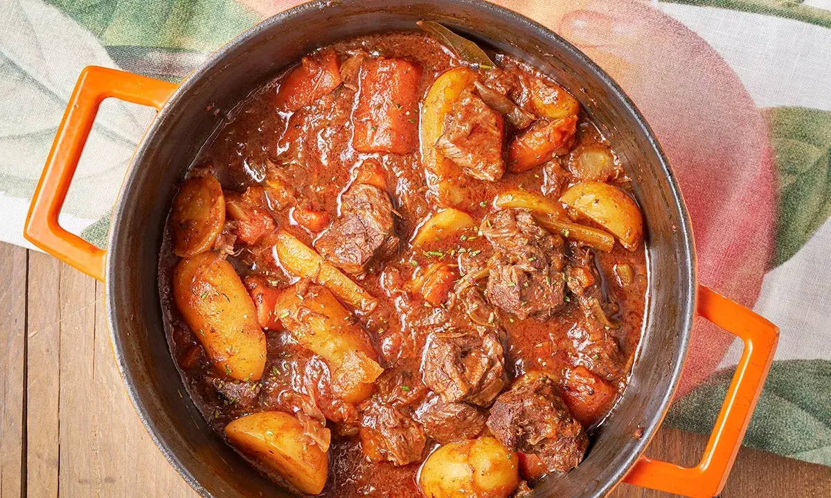 Un saporito spezzatino con patate, cotto lentamente in un tegame arancione, pronto per essere gustato.