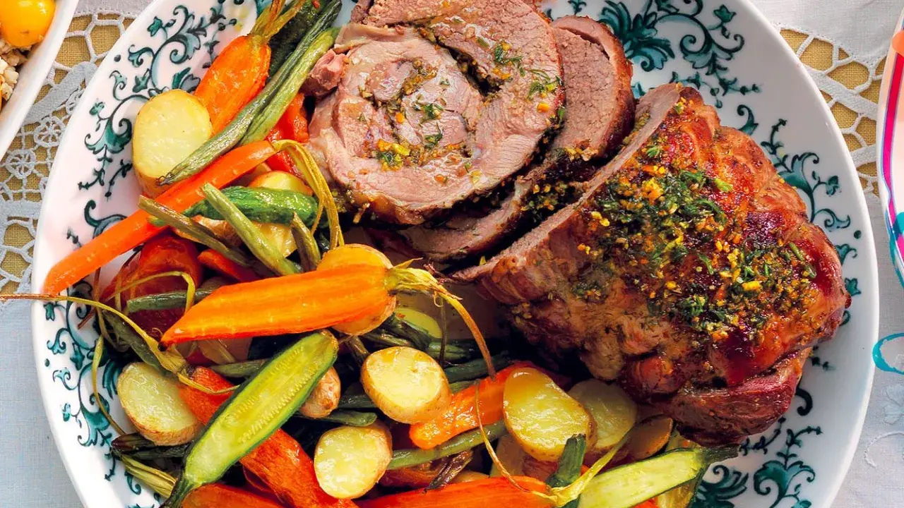 Un succulento agnello al forno, affettato e guarnito con erbe aromatiche, servito con patate novelle, carote e fagiolini.