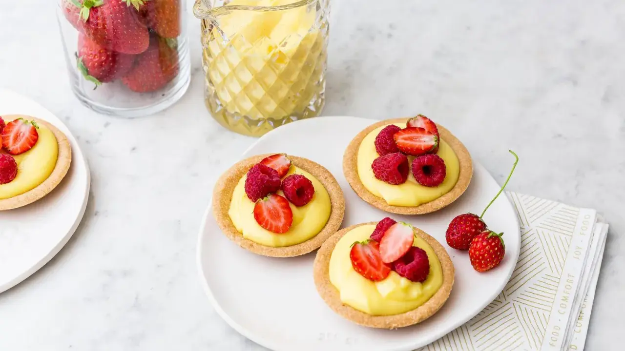Deliziose tartellette alla frutta con crema pasticcera e frutti di bosco freschi, pronte per essere gustate.