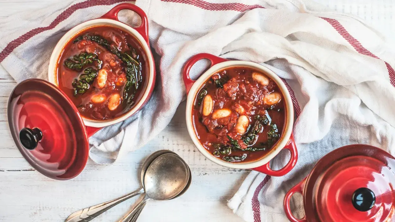 Due ciotole rosse con zuppa di cavolo nero e fagioli, pronte per essere gustate.