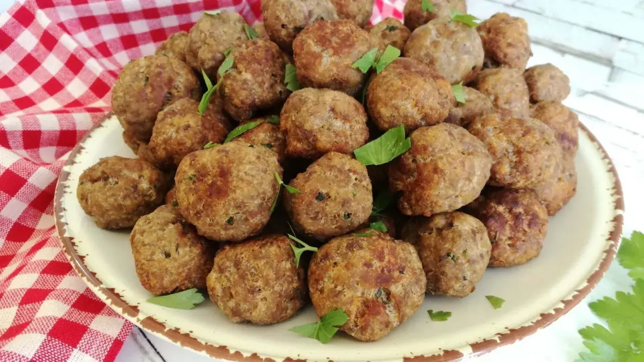 Un piatto colmo di polpette in bianco, dorate e profumate, guarnite con prezzemolo fresco.