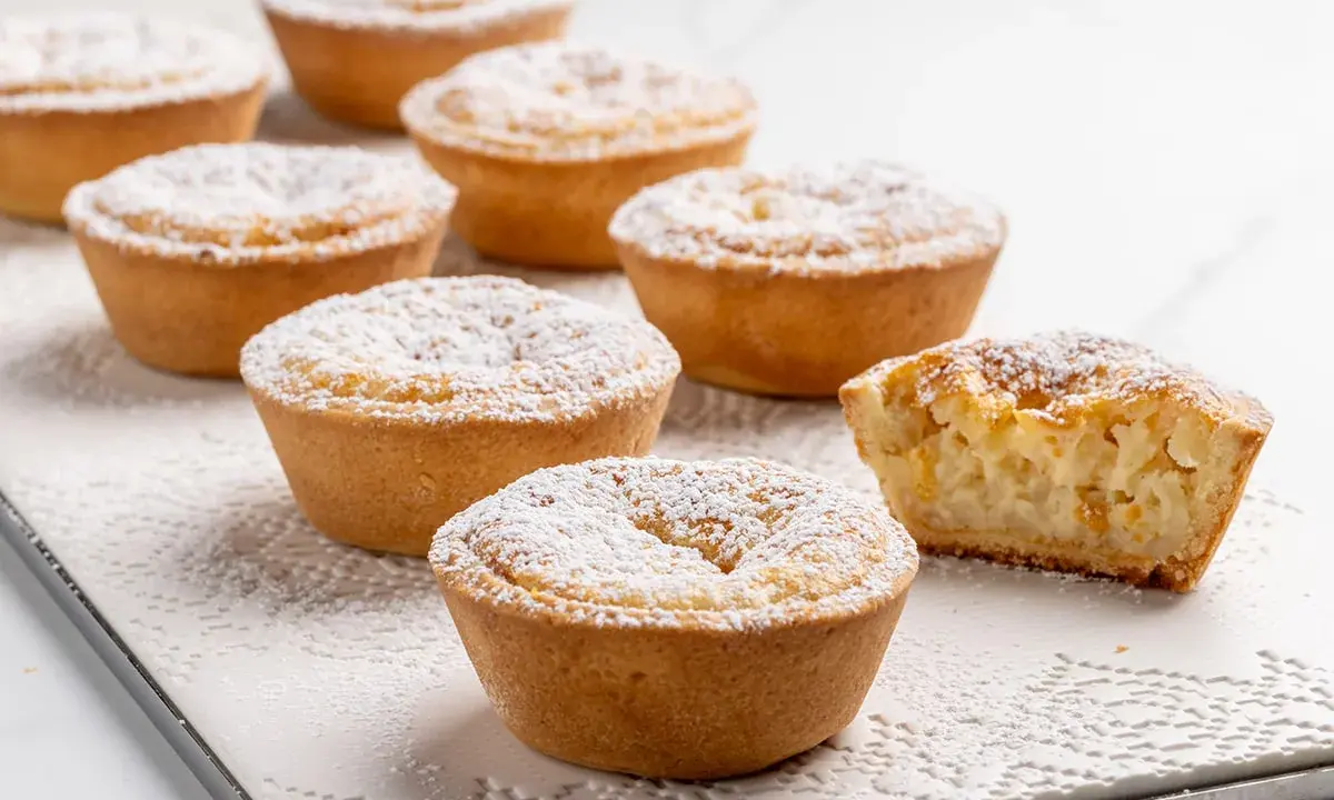 Deliziosi budini di riso in crostatina, spolverati di zucchero a velo. Uno è stato morso, rivelando il ripieno cremoso.