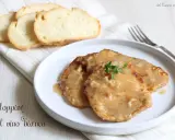 Tre scaloppine al vino bianco su un piatto bianco, guarnite con timo fresco, accompagnate da fette di pane tostato.