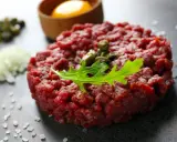 Tartare di manzo fresca, guarnita con capperi e rucola, pronta per essere gustata con tuorlo d'uovo e cipolla.