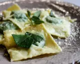 Ravioli ricotta e spinaci, conditi con burro fuso e foglie di salvia fresca, spolverati di parmigiano grattugiato su un piatto elegante.