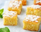 Deliziosi quadretti di torta al cocco, guarniti con scaglie di cocco e foglioline di menta fresca.