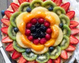 Torta alla frutta coloratissima, con fragole, kiwi, mandarini, lamponi e mirtilli disposti a raggiera su una base croccante.