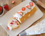 Rotolo panna e fragole decorato con panna montata e fragole fresche, pronto per essere gustato.